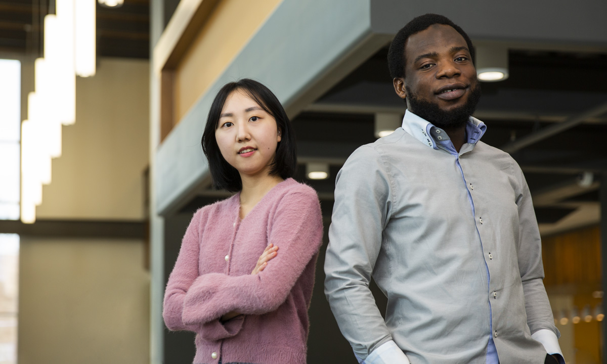 照片中，一位大学女生站在一位大学男生旁边，两人都微笑着看着镜头。