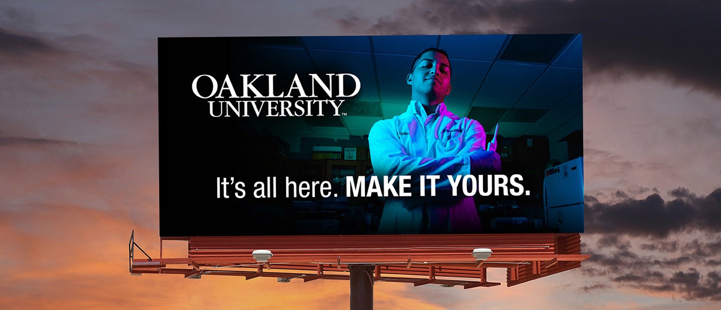 一个青年的广告牌和“奥克兰大学。万博ManBetX登录都在这里了。让它你的。”